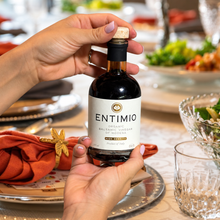 Hands holding an Entimio organic balsamic vinegar bottle at a dining table